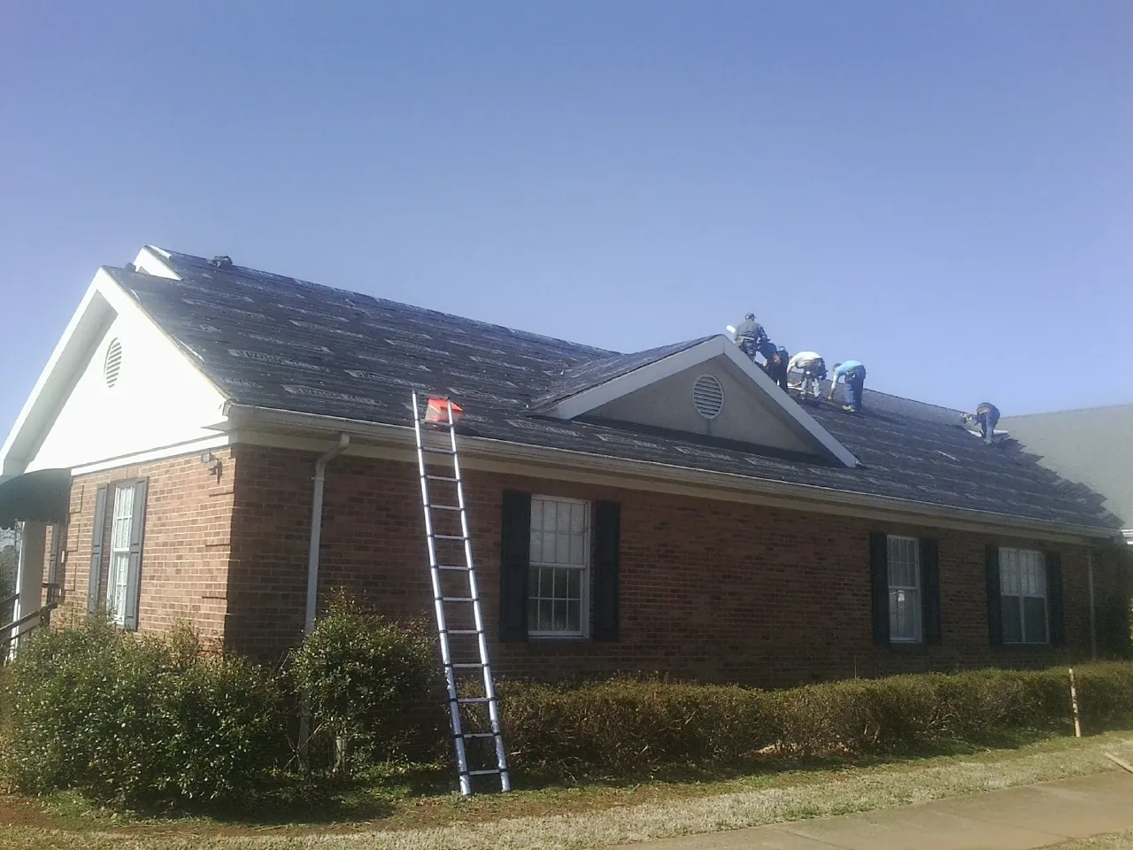 Crew tearing shingles off a brick ranch roof with a ladder set — Metal Roof Repair work by our crew in Oakland