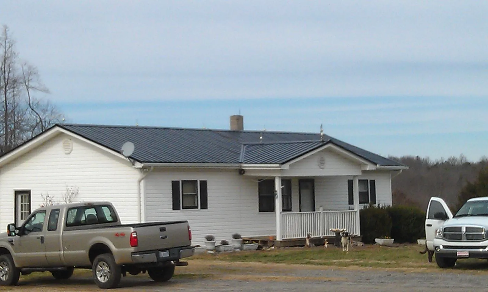 Finished dark metal roof on a white ranch home with work trucks parked in Oakland
